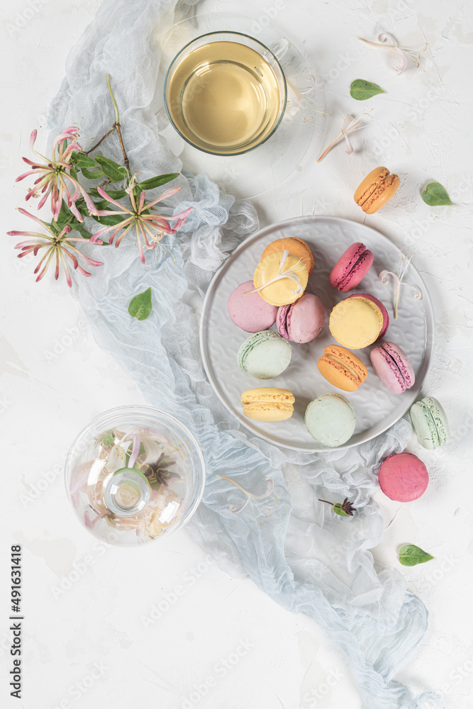 Colorful french macaroon cakes. Macaroons with jasmine flowers and tea on white table background. Selective focus Colorful french macaroon cakes. Macaroons with jasmine flowers and tea on white table background. Selective focus