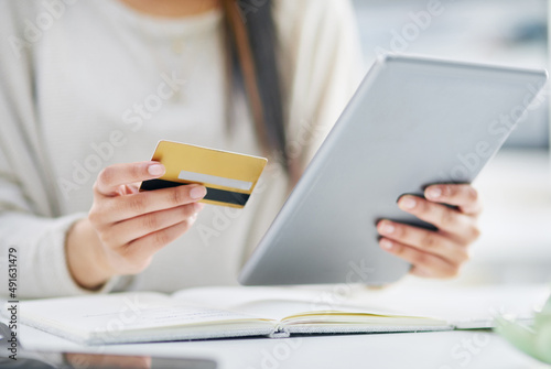Making a few quick swipes online. Closeup shot of an unrecognisable businesswoman using a digital tablet and credit card in an office.