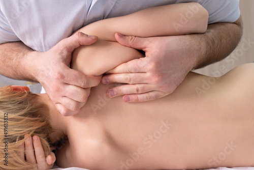 The osteopath works with a spatula. Back view. The teenage child lies on its side. The chiropractor works with the area of the thoracic region. Posture correction