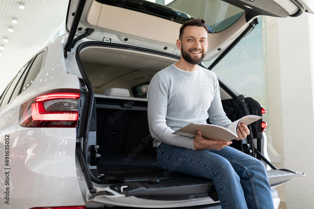 buying a new car in a car dealership, a man sits in the trunk of a car