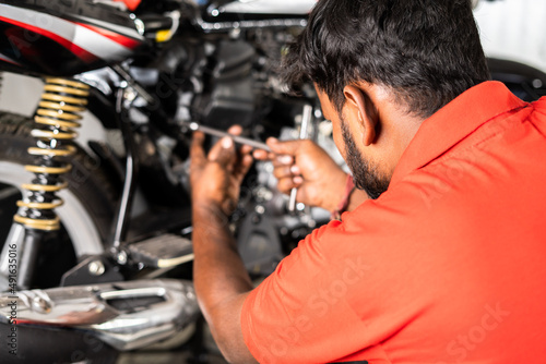 shoulder shot of focus on mechanic, motorbike mechanic fixing or reparing engine of motorbike at garage with copy space - concept of Hard working, maintenance service and occupation.