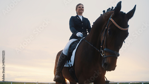 a beautifully trained smiling young woman rides a horse with her head bowed. High-quality photo