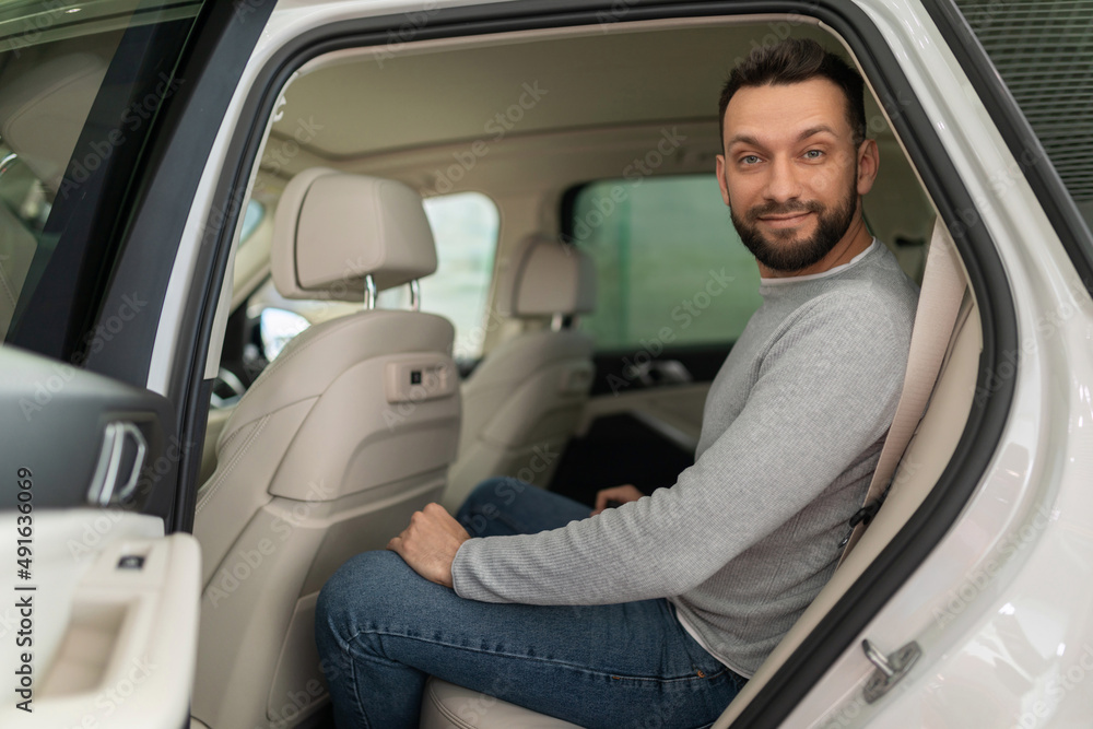 a customer in a car dealership sits in the back seat of a car with a smile on his face