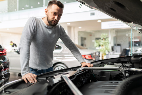 a man before buying a car inspects the engine compartment and examines the characteristics of the car