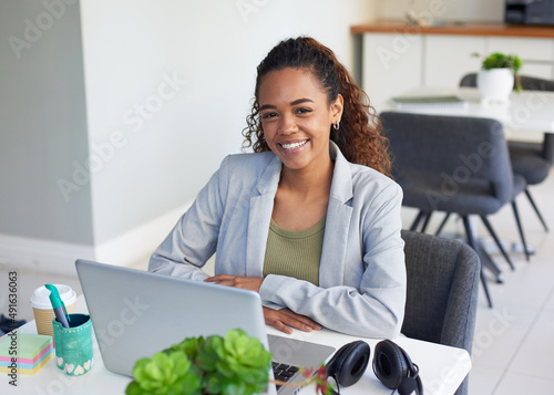 A young woman sits at her desk in a corporate office in front of her laptop photo