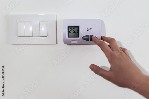 Close up view of a hand adjusting the heating temperature. Digital thermostat on the wall of the house