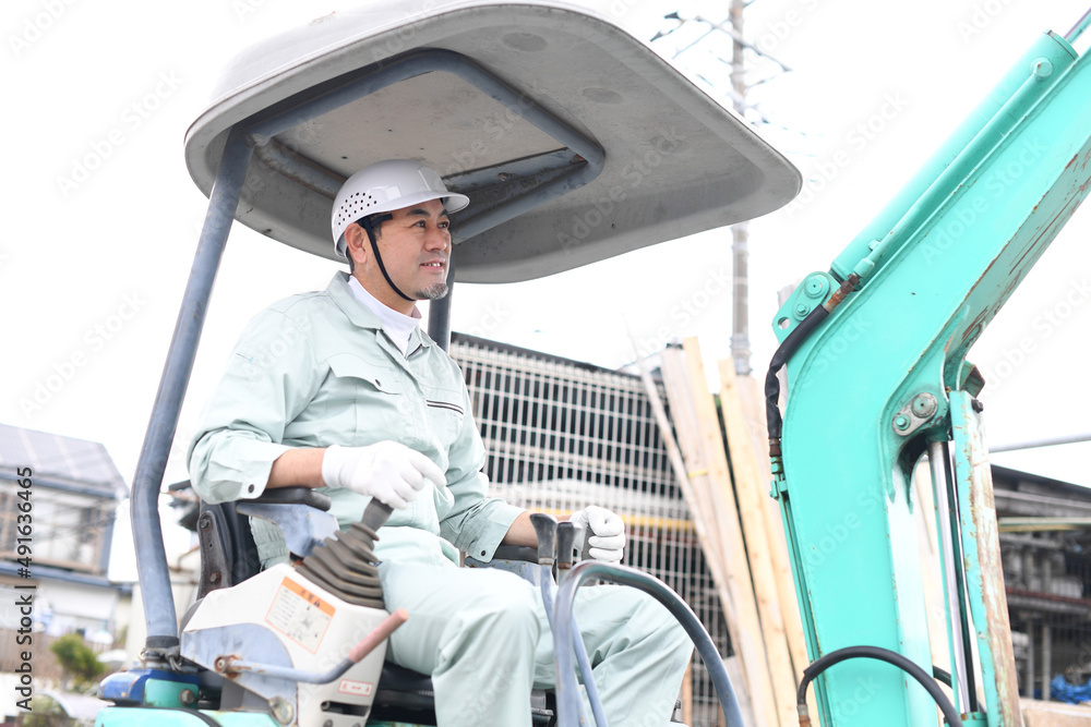 工事現場で重機に乗る作業員の男性 工事現場で重機に乗る作業員の男性
