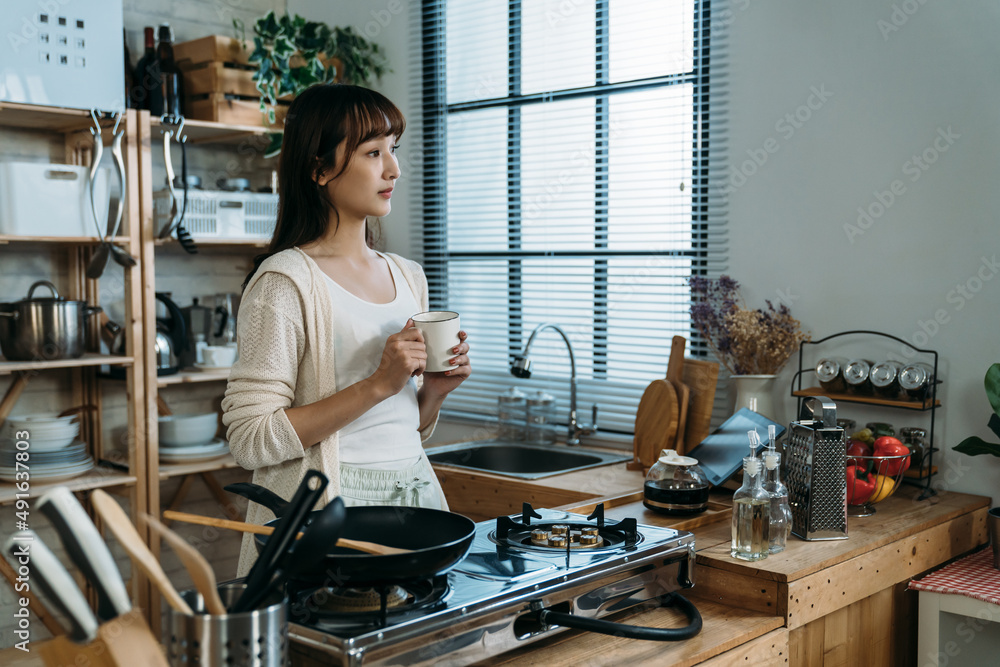 An Asian young housewife enjoy the break after children went to school, looking outside and holding the cup for the hot milk for relaxtion. An Asian young housewife enjoy the break after children went to school, looking outside and holding the cup for the hot milk for relaxtion.