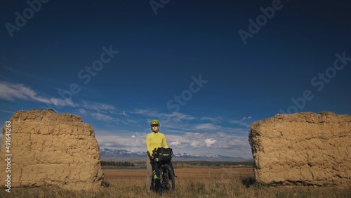 The woman travel on mixed terrain cycle touring with bikepacking. The traveler journey with bicycle bags. Sport bikepacking, bike, sportswear in green black colors. Mountain snow capped, stone arch. photo