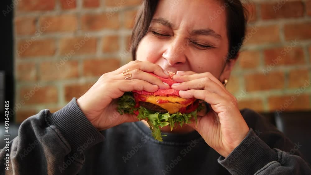 Young woman bites tasty burger in restaurant. Woman eating delicious vegan burger high quality 4K footage. Thailand. Young woman bites tasty burger in restaurant. Woman eating delicious vegan burger high quality 4K footage. Thailand.