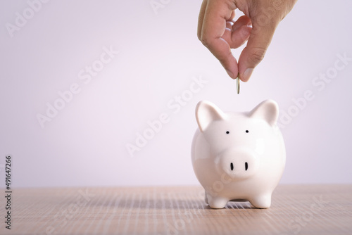 Hand putting coin into piggy bank. Business saving money wealth and financial concept finance, investment, Financial planning. on wooden table and white background with copy space for text.