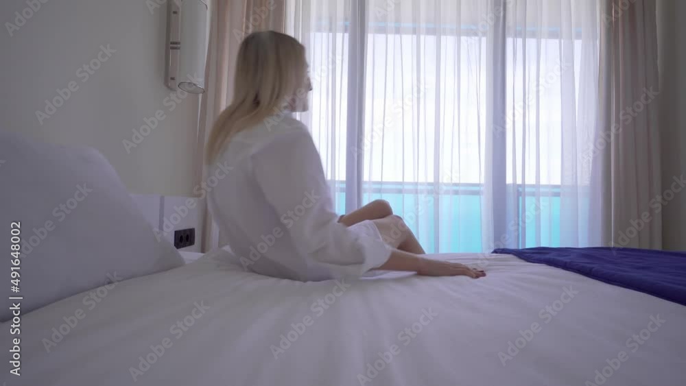 Beautiful blonde, wakes up in morning, gets out of bed and stretches in front of window. happy young girl greets new day with warm flash of sunlight. In white shirt with bare legs in underpants. Beautiful blonde, wakes up in morning, gets out of bed and stretches in front of window. happy young girl greets new day with warm flash of sunlight. In white shirt with bare legs in underpants.
