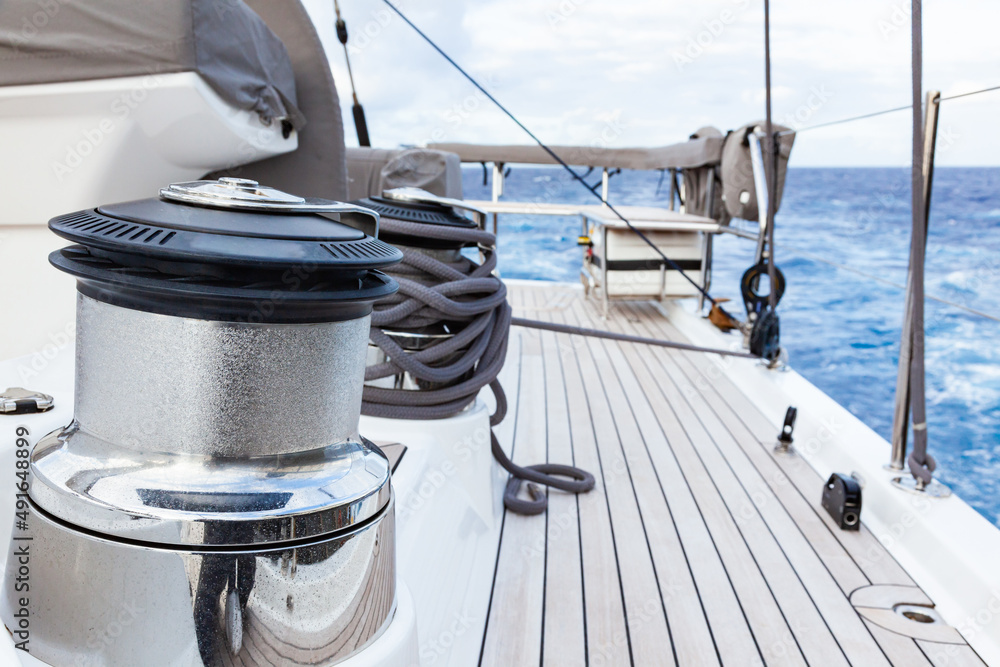 Fototapeta premium Part of the teak deck of a sailing yacht with bollards and sail winches for fixing the sail ropes.