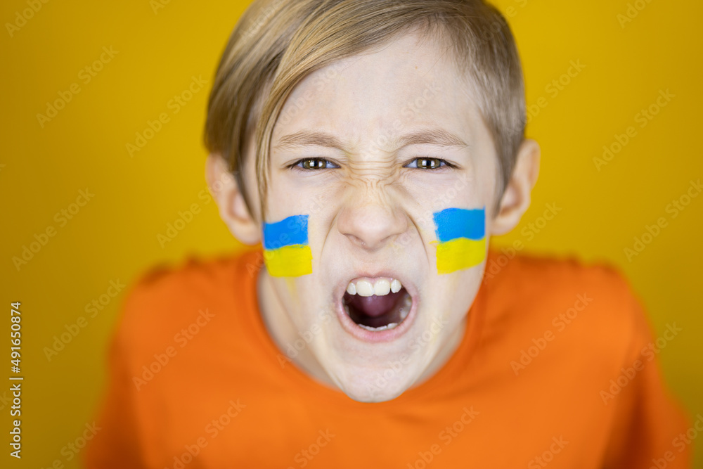 a boy with a painted flag of Ukraine on his cheeks shouts angrily at the camera against the war