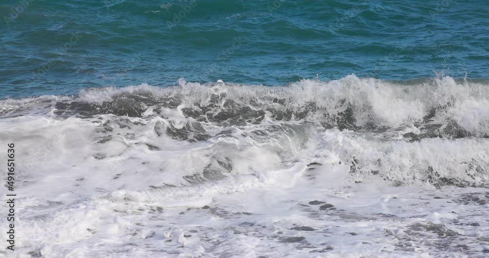 Crashing wave coming straight in with seaspray on black stone beach in slow motion Crashing wave coming straight in with seaspray on black stone beach in slow motion