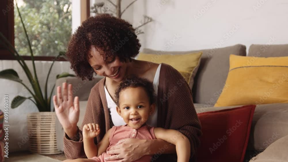 Portrait of biracial female and young child waving at camera while sitting on floor in modern-styled living room in the daytime Portrait of biracial female and young child waving at camera while sitting on floor in modern-styled living room in the daytime