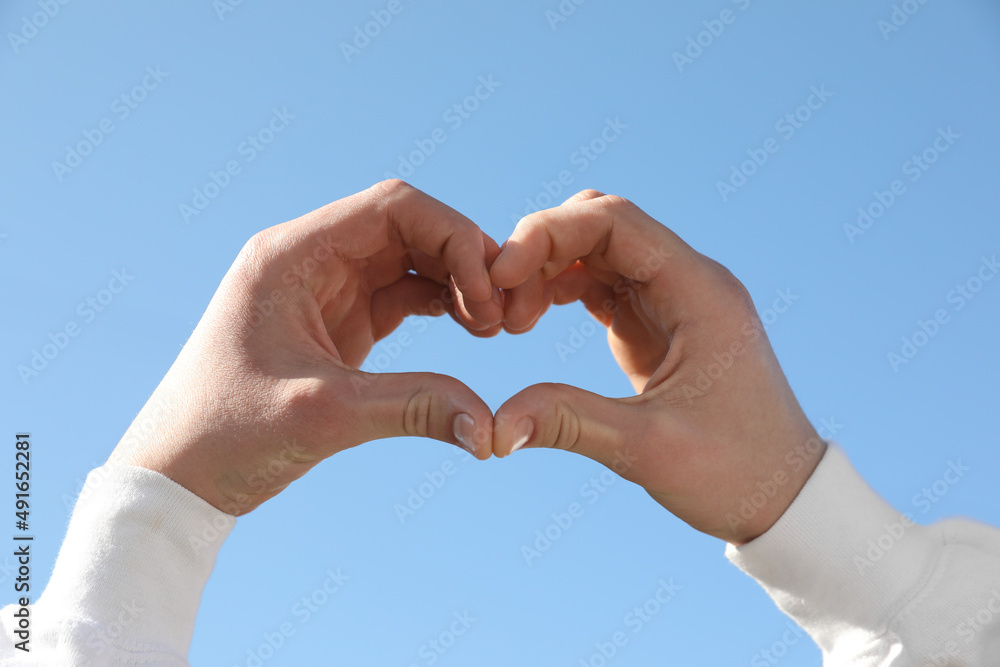 Man showing heart against blue sky outdoors on sunny day, closeup of hands Man showing heart against blue sky outdoors on sunny day, closeup of hands