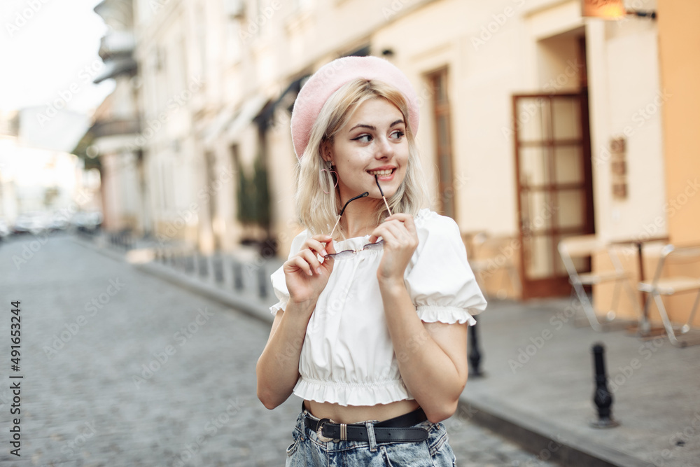 Fototapeta premium Portrait of a charming young woman in a beret and glasses on European street