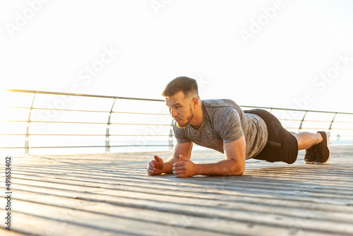 Foto Athletic man in sportswear practicing plank on the beach in the early morning