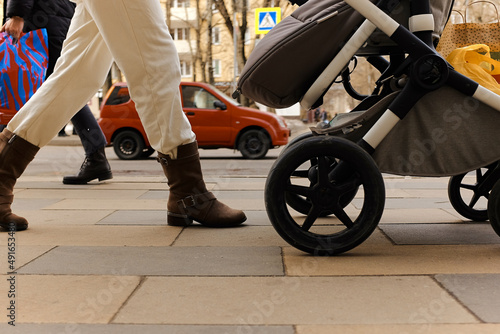 Stylish woman walks with stroller, goes from store with purchases, red car drives by, busy traffic on sidewalk