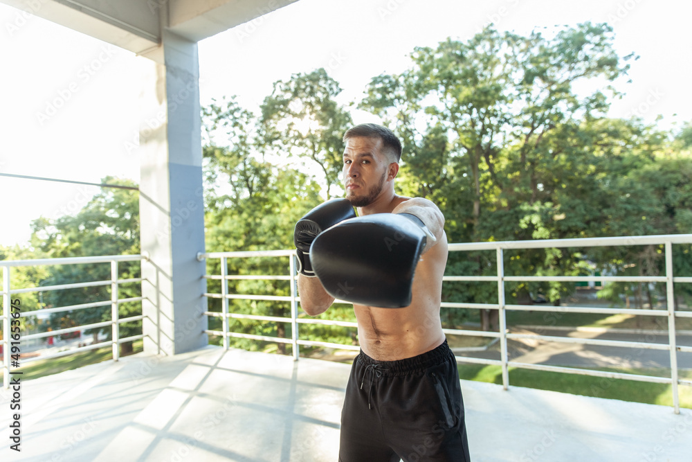 Naklejka premium Muscular man training punches with boxing gloves outdoors