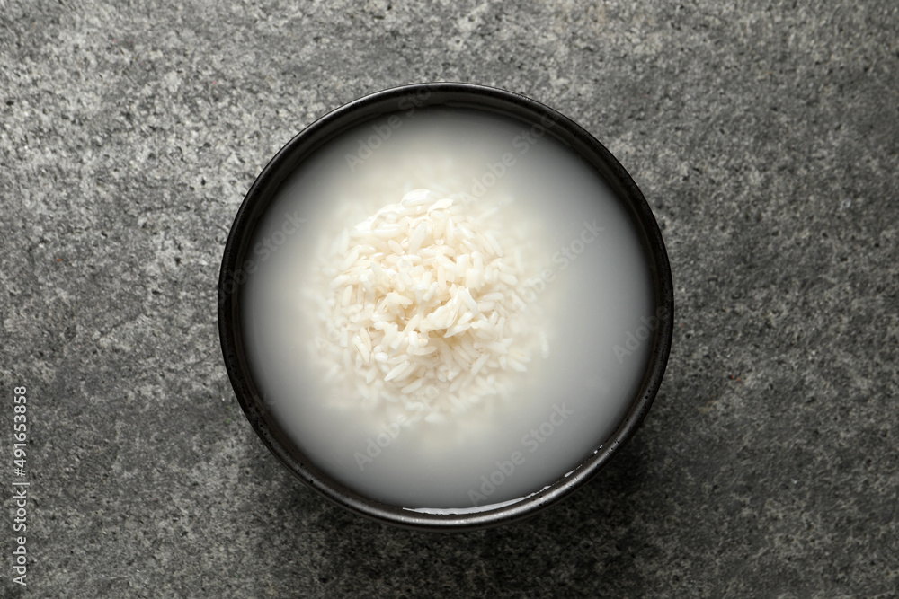 Bowl with rice soaked in water on grey table, top view Bowl with rice soaked in water on grey table, top view