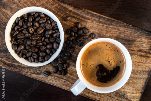 Close-up of hot black coffee in white coffee cup and roasted coffee beans in white bowl on wooden background. Top view © Ivan