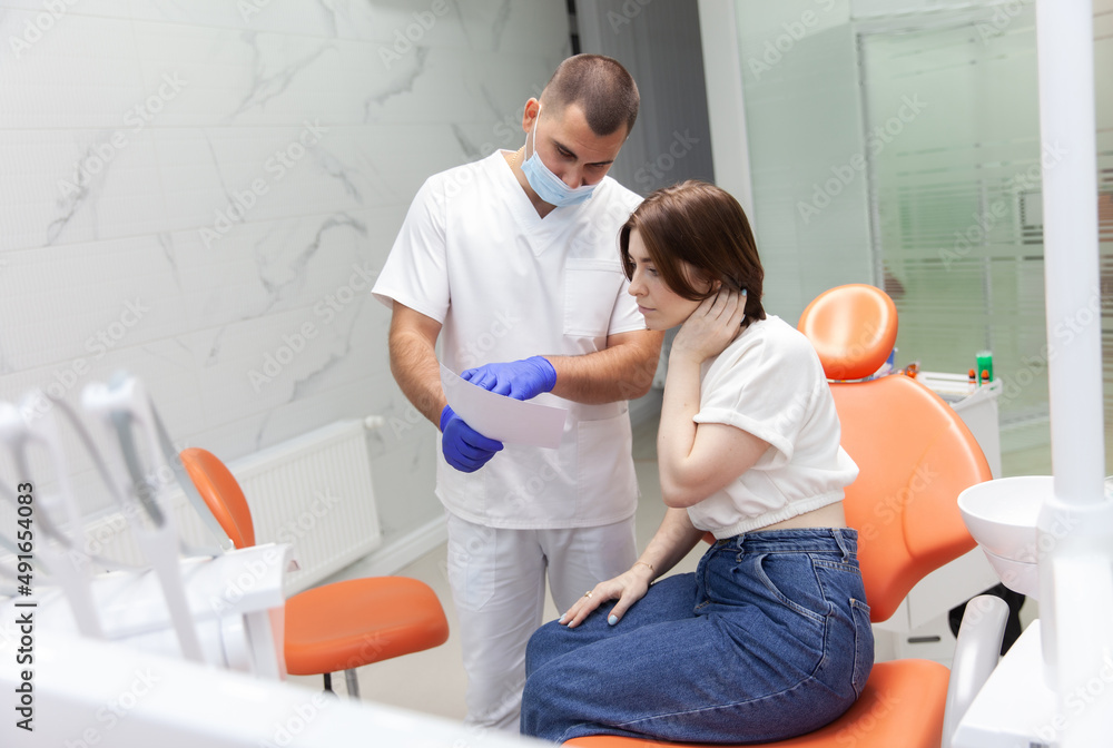 Professional doctor dentist shows a picture of teeth to a woman sitting in a chair to a patient Professional doctor dentist shows a picture of teeth to a woman sitting in a chair to a patient