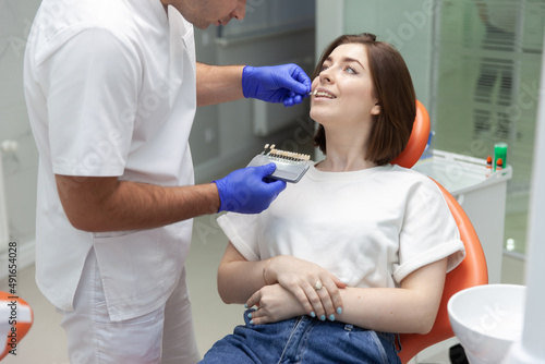 Professional dentist selects the color tone of the teeth for the female patient in the dental clinic