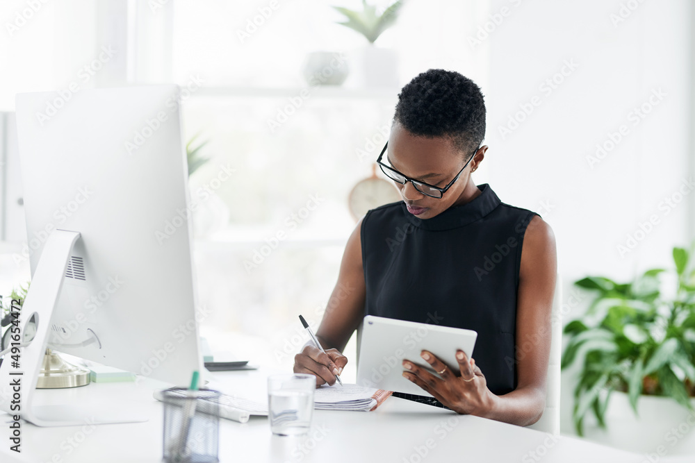 Fototapeta premium Stay organised, stay in control. Shot of a confident young businesswoman writing in a notebook and using a digital tablet in a modern office.