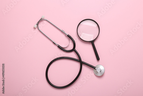Stethoscope with magnifying glass on pink background. Diagnosis of diseases. Top view