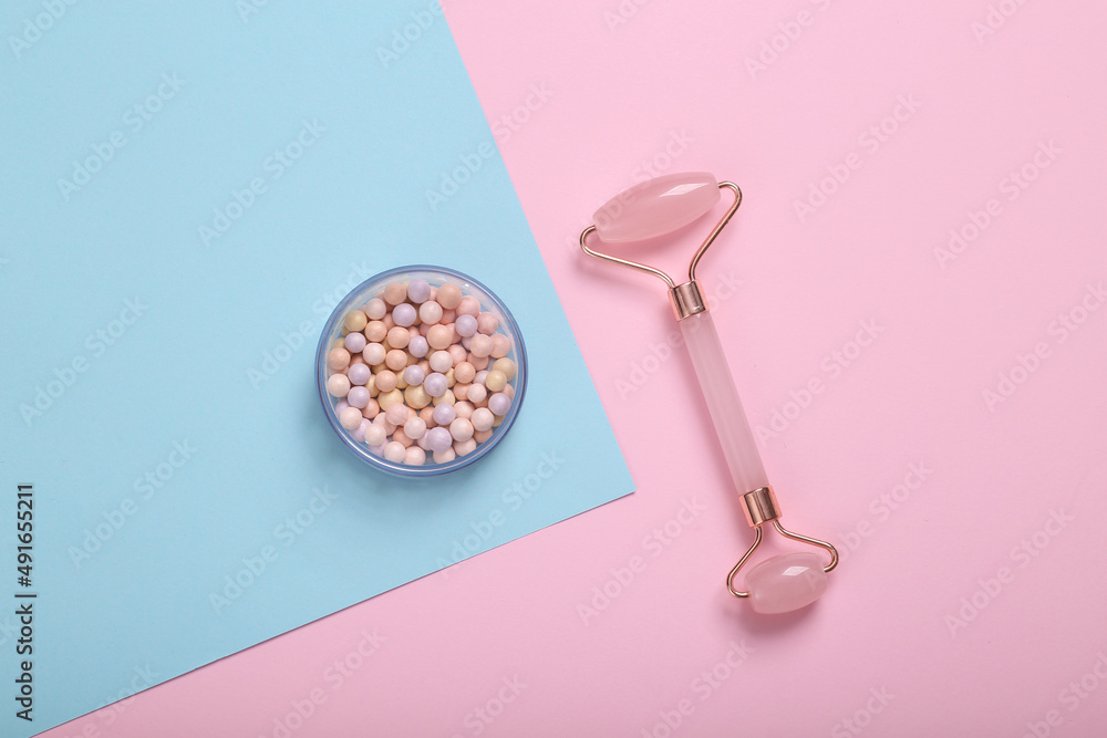 Facial massage roller and balls of powder on blue pink pastel background. Top view Facial massage roller and balls of powder on blue pink pastel background. Top view