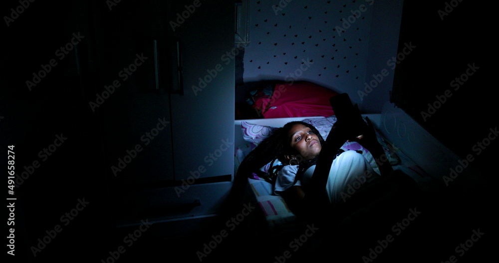 Teen black girl using cellphone device at night in bed Teen black girl using cellphone device at night in bed
