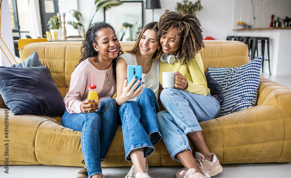 Three young multiracial women taking selfie while relaxing together at home - Female millennial friends sitting on sofa and having fun at weekend - Friendship and happiness concept Three young multiracial women taking selfie while relaxing together at home - Female millennial friends sitting on sofa and having fun at weekend - Friendship and happiness concept