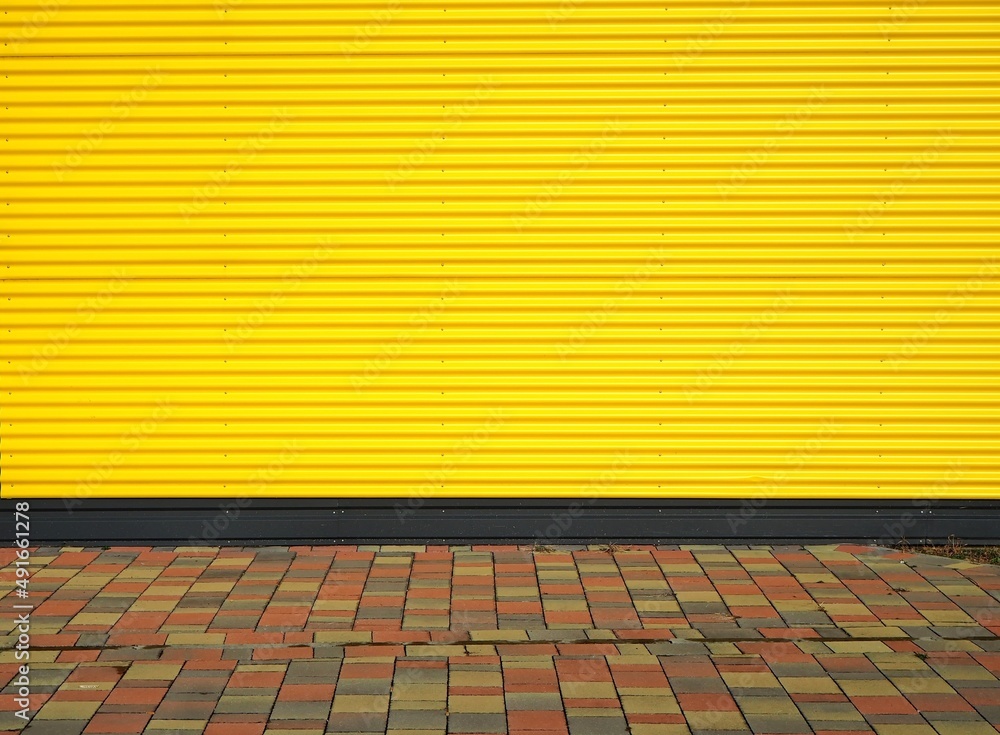 Yellow striped aluminium cladding wall and a  tiled pavement with different colors. Background and texture, copy space