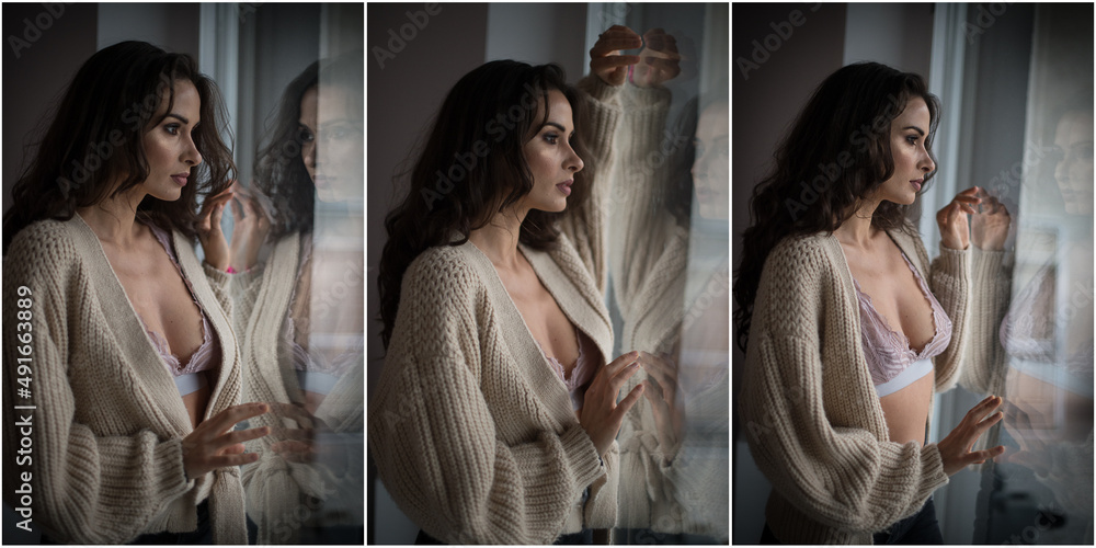Attractive sexy brunette in white bra and brown sweater posing provocatively, near a window,studio shot. Portrait of sensual woman with long hair, in classic boudoir scene , looked out the window