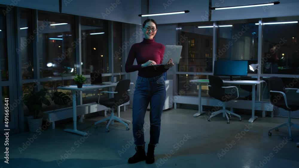Full-length view of asian businesswoman work on laptop standing in dark empty office Full-length view of asian businesswoman work on laptop standing in dark empty office