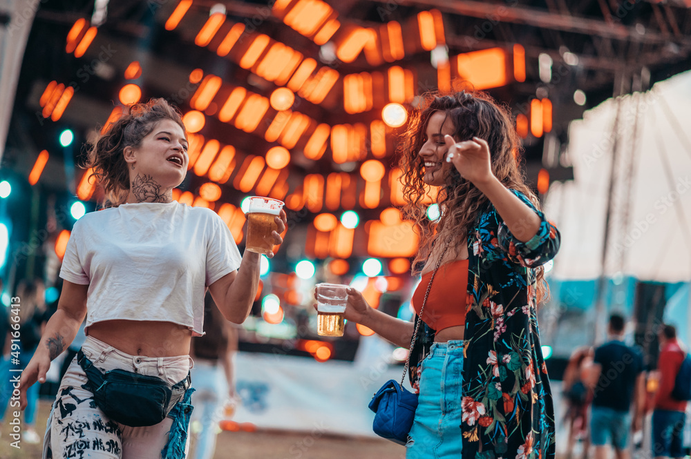 Two beautiful friends drinking beer and having fun on a music festival