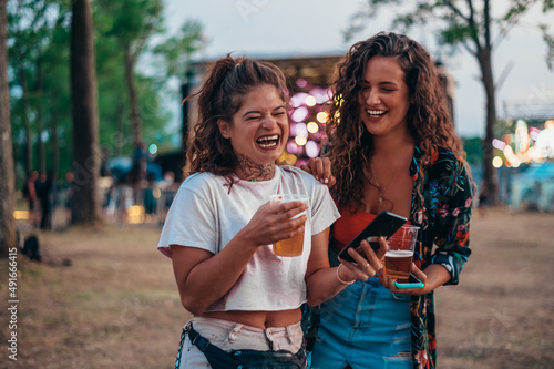 Two beautiful friends using a smartphone on a music festival