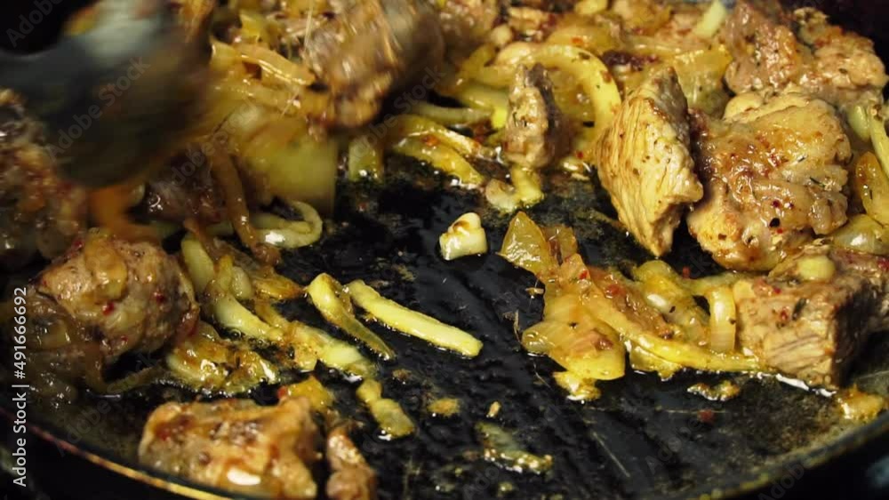 A woman's hand turns over fried pork meat in a frying pan. A housewife cooking fried meat with onions in the kitchen on a gas stove. Food in the form of stewed pieces of meat and onions. Protein