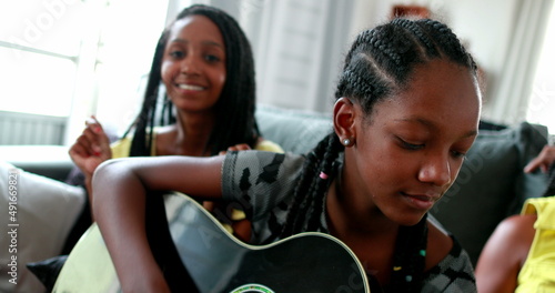 Happy African family enjoying music. Teen daughter playing guitar for parents and siblings