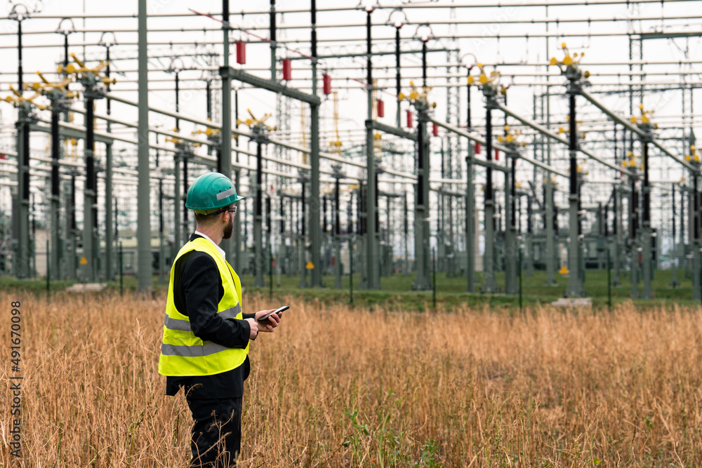 custom made wallpaper toronto digitalElectric engineer wearing helmet suit and safety vest at bad weather checking datas on tablet with substation in background