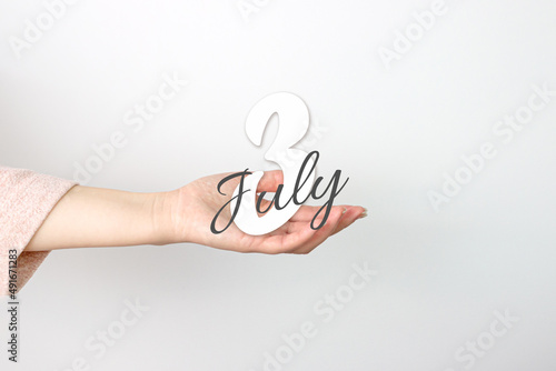 July 3rd. Day 3 of month, Calendar date. Calendar Date floating over female hand on grey background. Summer month, day of the year concept.