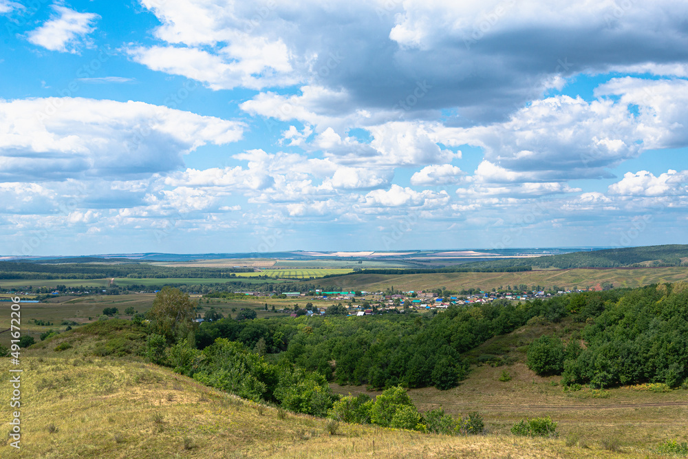 Fototapeta premium Hills, sky with clouds and a village in the distance.