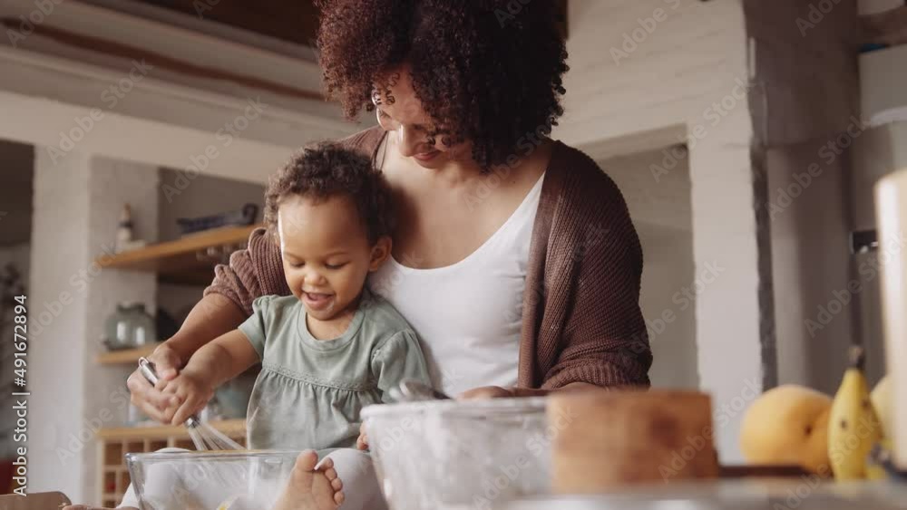 Biracial mother whisking egg with her daughter while baking in a modern-styled kitchen. Biracial mother whisking egg with her daughter while baking in a modern-styled kitchen.