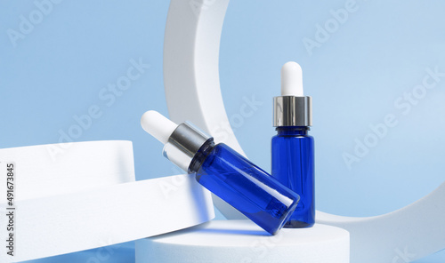 Blue glass dropper bottles on round form on blue background. Cosmetic container mock-up. Background for branding and packaging presentation. Natural skincare beauty product concept