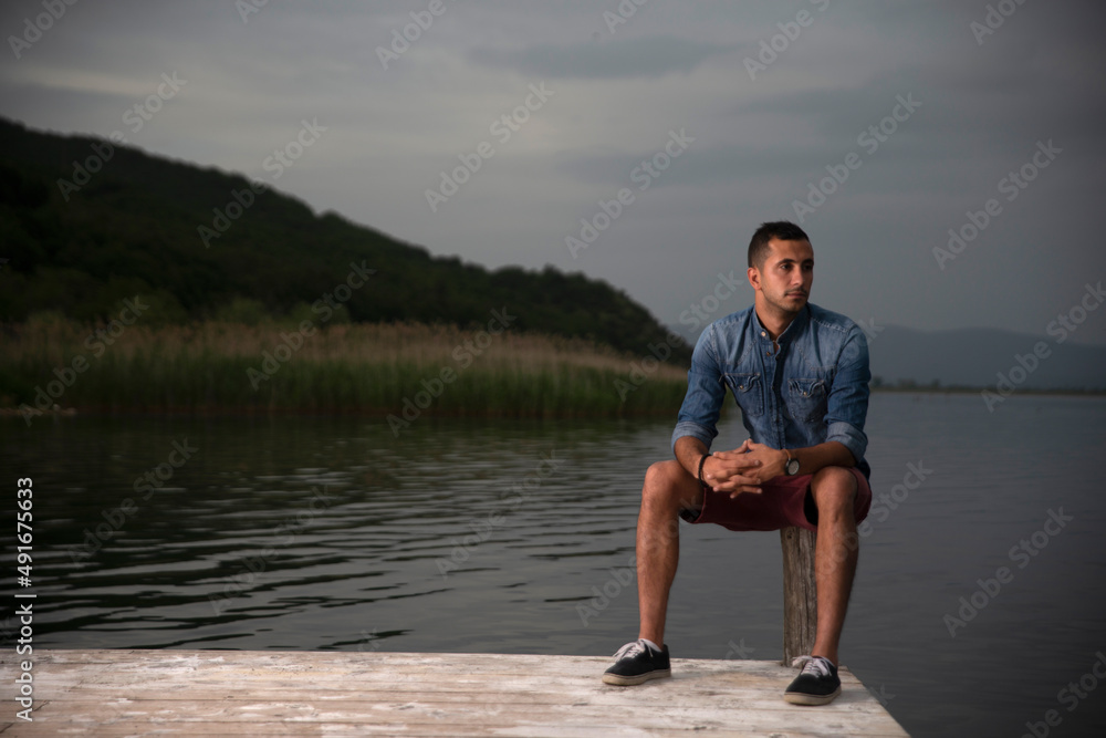 Fototapeta premium Fashion portrait of young man in denim shirt poses over wall with contrast shadows