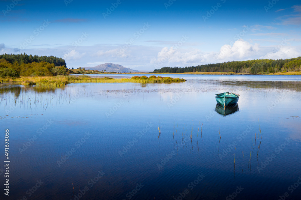 An isolated rowing boat sits on a calm lake with beautiful blue lake and sky