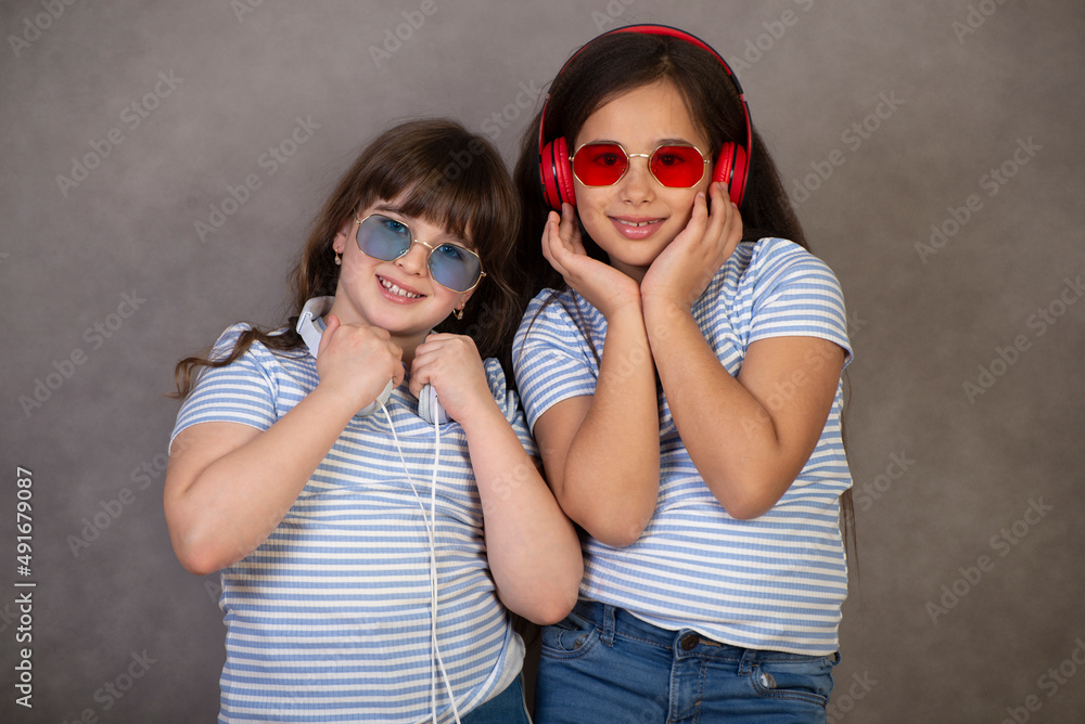 Portrait of two cute, charming, cute little girls who are happy and having fun in the studio on a gray background Portrait of two cute, charming, cute little girls who are happy and having fun in the studio on a gray background