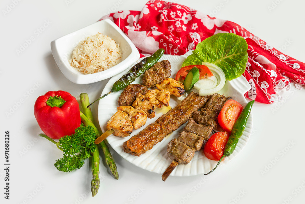 Selection of BBQ chicken tikka and seekh kebabs served with rice salad in a dish isolated on colorful table cloth top view on grey background Selection of BBQ chicken tikka and seekh kebabs served with rice salad in a dish isolated on colorful table cloth top view on grey background
